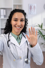 Vertical shot, female doctor smiling joyfully waving at phone camera, talking to patients remotely...