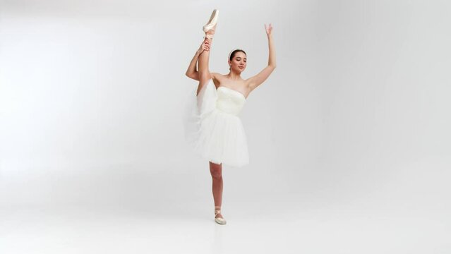 A professional ballerina in a white tutu dances in a large training hall. A girl makes dance steps in a stage dress. Shot against a white background in a spacious studio.