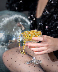 Champagne glass full of golden Christmas beads as Non-alcoholic drink in person hand with disco...