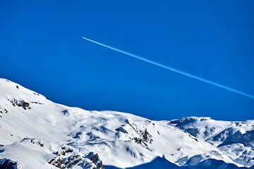 Verschneite Berge und ein Flugzeug am Himmel