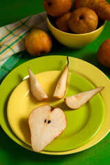 Green plate with slices and half of pear and green kitchen towel on green wooden background..