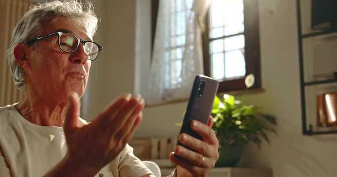 At home, a middle-aged man makes a video call to her relatives and friends using his smartphone. The elderly man smiles, blows kisses and is happy to talk to them.