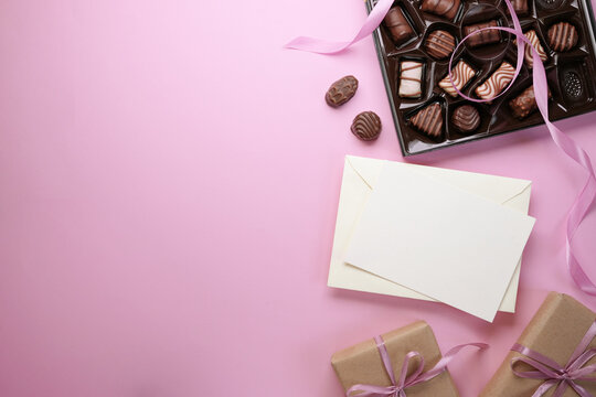 Top view photo of open pastel yellow envelope with paper sheet with chocolate candies on pink background with blank space. Flat lay. Lover's holiday confession or proposal concept. 