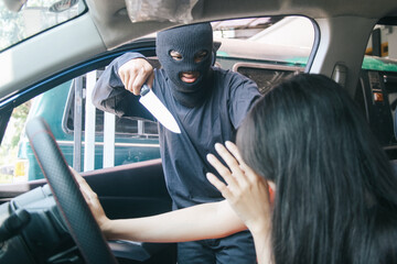 Thief in balaclava holding a knife burglarize to steal the car from woman  - obrazy, fototapety, plakaty