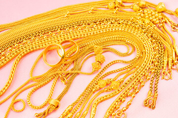 Group of gold necklaces on pink fabric background.