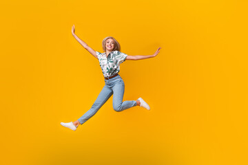 Fototapeta na wymiar Full size photo of positive girl dressed print shirt stylish jeans flying hold palms like wings isolated on yellow color background