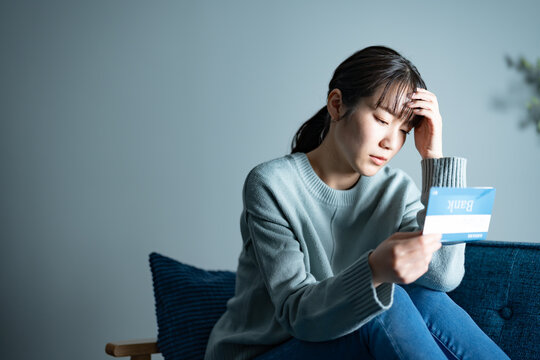 ソファに座り通帳を持ち落ち込む女性