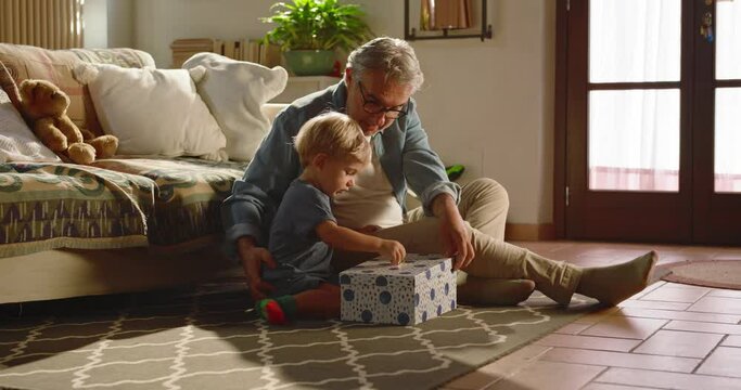 At home, the grandfather gives his grandson a gift.
In the living room, the child unwraps the gift and when he opens it he is very happy with the surprise