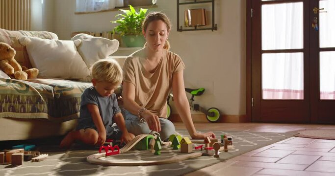 At home, at sunset, the mother and his beautiful son play with a wooden train and teaches him to build the track to play while they have fun