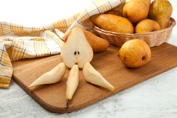 Cutting board with whole and slices pears, wicker basket and yellow kitchen towel on white wooden background..