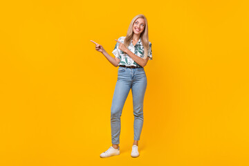 Fototapeta na wymiar Full size photo of cute gorgeous girl dressed print shirt jeans look directing at offer empty space isolated on yellow color background