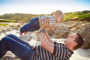 Young father playing with baby son as lying at the beach