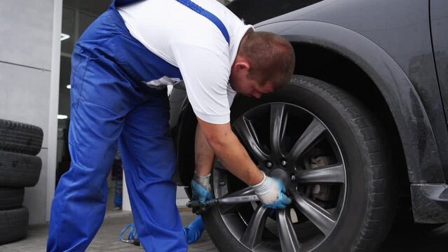Auto mechanic secures car wheel with torque wrench for precision. Worker in uniform installs tire ensuring safety, reliability in automotive repair shop scenario. Professional car maintenance task.