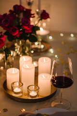 Candlelight date in restaurant. Glasses with wine, bouquet flowers. Romantic dinner setup at night. Table setting for couple, Valentine's Day evening, burning candles for surprise marriage proposal.