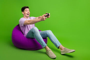 Full length photo of positive carefree man sitting comfy pouf watching playstation empty space...