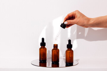 Serum or essence glass three bottles on the mirror and womans hand with a pipette above them.