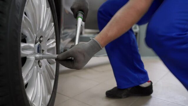 Auto mechanic in blue uniform tightens cars alloy wheel with torque wrench at modern auto repair shop. Skilled technician ensures safety, precision luxury vehicle maintenance.