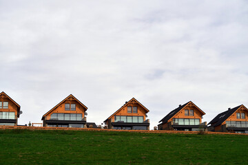 Fototapeta na wymiar Cozy wooden homes with balconies and windows that offer a panoramic view of the green landscape and the cloudy sky.