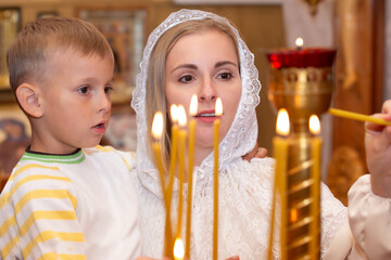 A mother and son light candles in an Orthodox church.