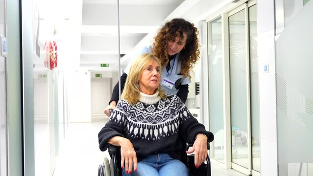 Nurse carrying a mature woman in wheelchair along the hospital corridor
