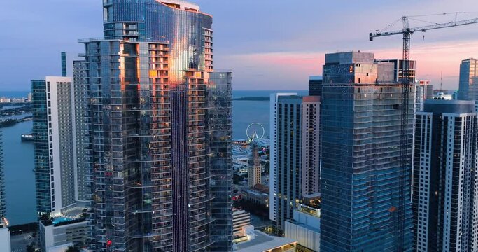 Glass tall modern buildings in Miami at sunset. Panorama of evening shining city on background of ocean. Reflections in windows.