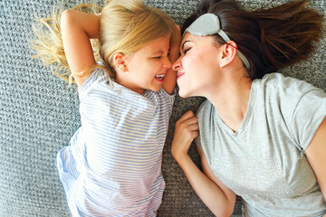 Cute loving emotional woman hugging her daughter tight while spending the morning in bed and feeling happy. Nose to nose