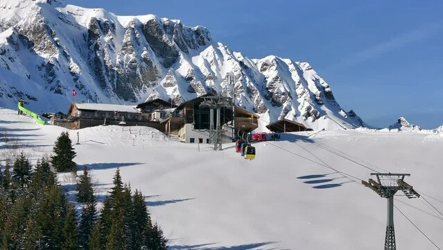 Colorful cable cars entering the mountain station Tschentenegg in Adelboden Switzerland on a sunny winter day. Zoomed drone shot
