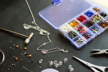 Box with colorful beads, string, wire, chain, scissors, pliers and hammer on dark background....