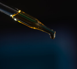 Glass pipette for cosmetics. A drop of cosmetics oil on a black background close-up macro