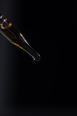 Glass pipette for cosmetics. A drop of cosmetics oil on a black background close-up macro