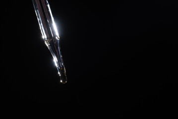 Glass pipette for cosmetics. A drop of cosmetics oil on a black background close-up macro