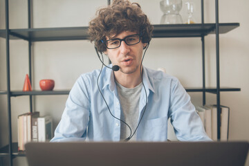 Male agent or telemarketing in eyeglasses with headphone talking to customer working at home. Man...
