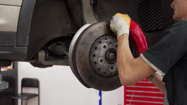 Auto mechanic replaces disc brakes and pads at car service. Technician works on vehicles brake system, ensures safety. Detail shot of hands, tools, and car components in maintenance.
