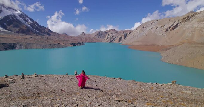 Filmy drone shot reveals Nepal landscape of Tilicho World's highest Lake, woman in pink dress walks with Heroine feels, cinematic blue sky with clouds 4K
