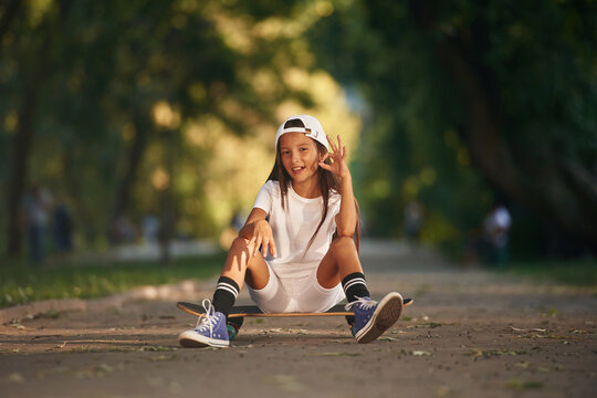 Chilling, sitting and relaxing. Happy little girl with skateboard outdoors