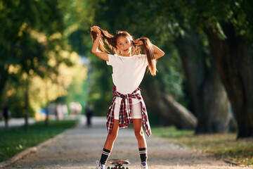 Playing with the hair, going crazy. Happy little girl with skateboard outdoors