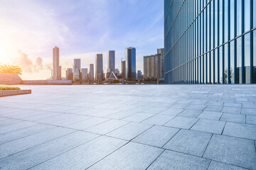 Empty square floor and glass wall with modern building at sunrise - obrazy, fototapety, plakaty