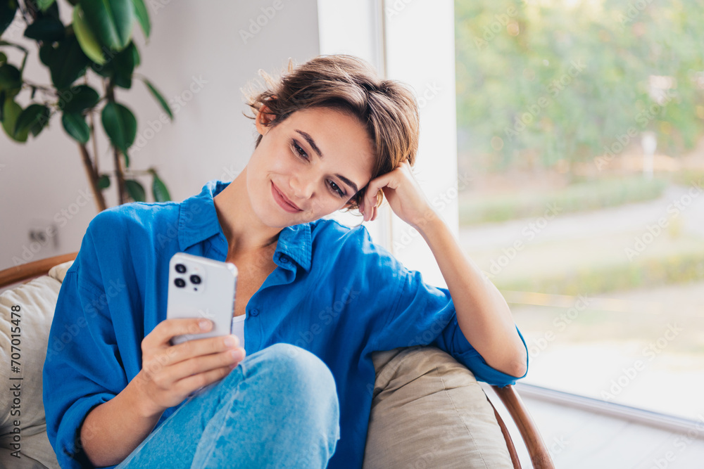 Wall mural photo of cheerful lovely girl sitting in comfy armchair writing answer online chat indoors