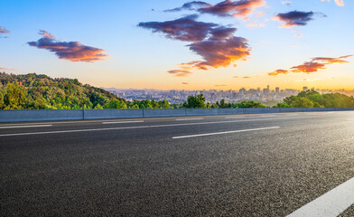 Asphalt road and green mountains with city skyline landscape at sunrise. high angle view.