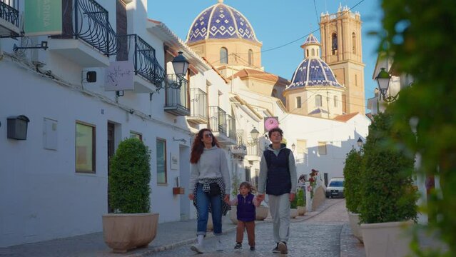 Family walking along a Spanish street in a small village with white houses. Spanish city of Altea in the city center on the mountain church with a blue roof. Tourists sightseeing