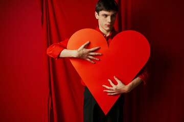 young man in black shorts embracing large heart shaped carton on red background, Valentines day