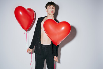 romantic young man in black open shirt holding red balloons on grey background, Valentines day - Powered by Adobe