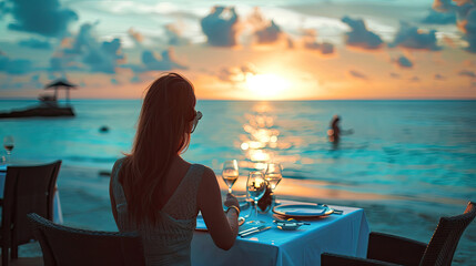 Romantic dinner on sunset. Woman sitting alone on table set with lantern for a romantic meal on beach, yachts and ocean on background. Dinner for a couple in love in luxury outdoor restaurant - obrazy, fototapety, plakaty