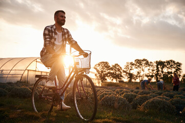 Riding bicycle. Handsome man in casual clothes is on the agricultural field near greenhouse