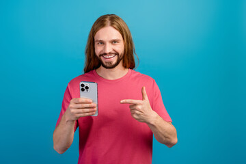 Photo of nice cheerful guy indicate finger hand hold apple iphone gadget isolated on blue color...