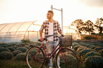 Standing, enjoying nature. Handsome man in casual clothes is with bicycle on the agricultural field...