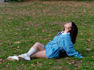 Fototapeta premium Beautiful young Chinese woman sitting on sunny summer meadows, wearing blue loose oversized top and miniskirt with small shoulder bag. Emotions, people, beauty, youth and lifestyle portrait.
