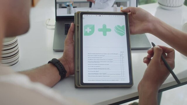 Back view of couple filling health questionnaire with yes or no answers using digital tablet at table
