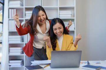 Excited asian business woman celebrating victory together on laptop computer in office.