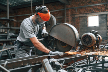 Process of cutting the metal. Young factory worker in grey uniform